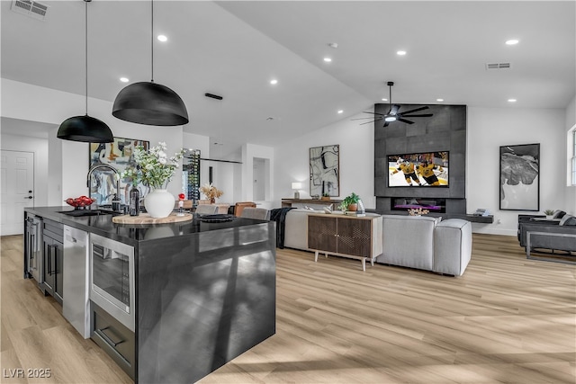 kitchen featuring visible vents, light wood finished floors, a sink, stainless steel microwave, and open floor plan