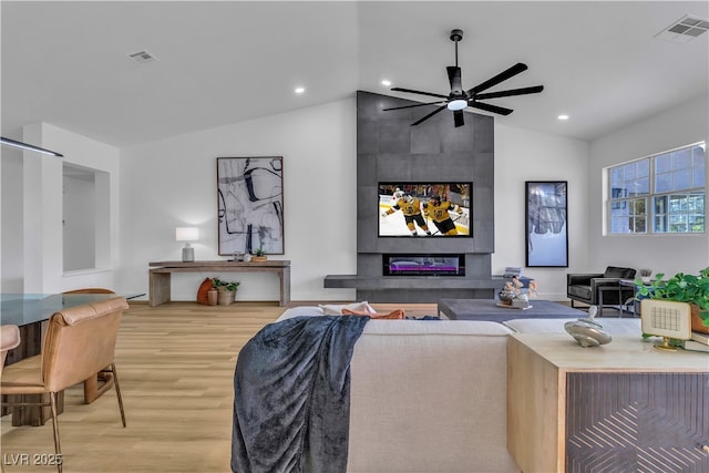 living room with vaulted ceiling, wood finished floors, visible vents, and a tile fireplace