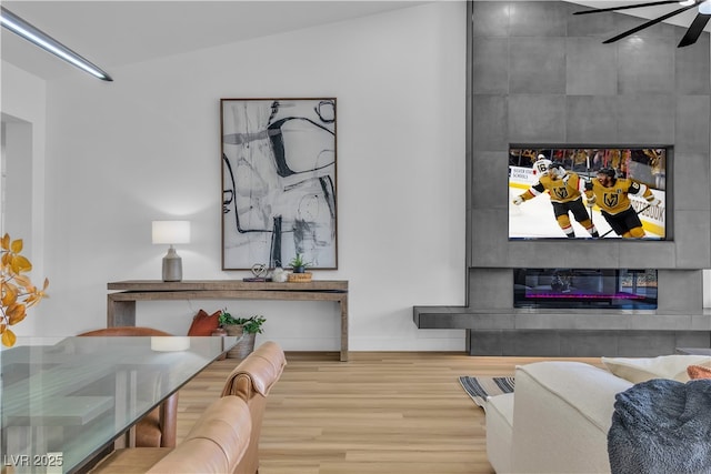 living room featuring a fireplace, baseboards, a ceiling fan, and wood finished floors