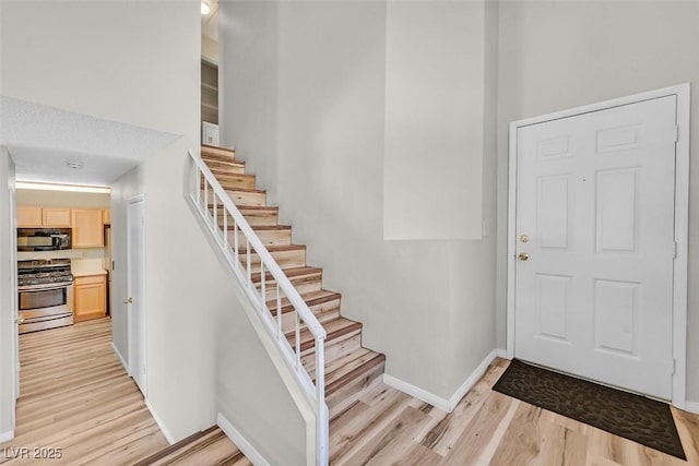 entrance foyer with stairway, light wood-style flooring, and baseboards