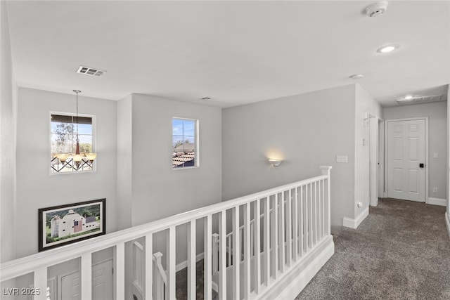 hall with carpet, visible vents, baseboards, and an upstairs landing