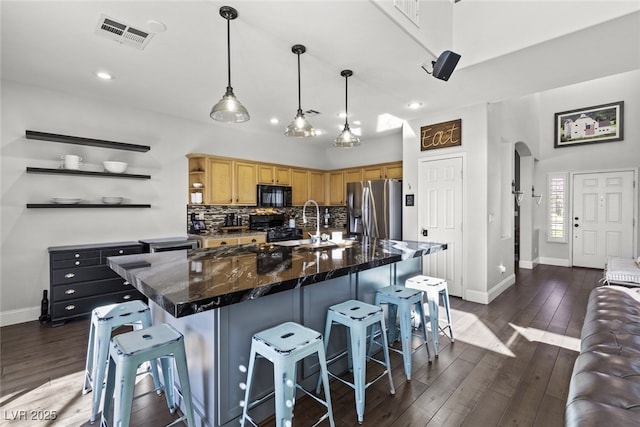 kitchen featuring visible vents, arched walkways, dark wood-style floors, black appliances, and backsplash