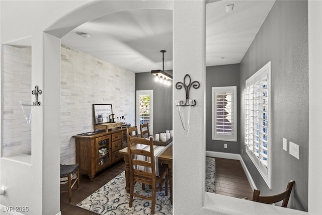 dining room featuring a textured wall, arched walkways, dark wood finished floors, and baseboards