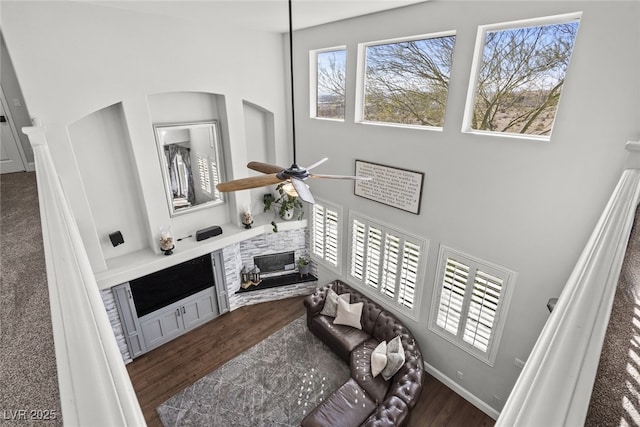 living area with dark wood-style floors, a high ceiling, a ceiling fan, and baseboards