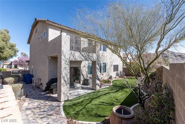 rear view of house with a fenced backyard, a tile roof, a lawn, stucco siding, and a patio area