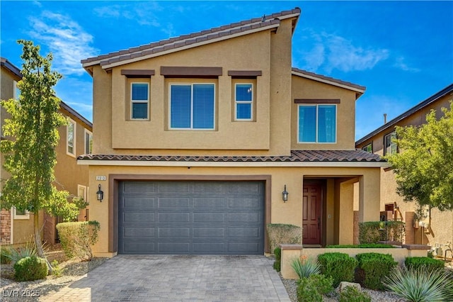 view of front facade featuring a garage, a tiled roof, decorative driveway, and stucco siding