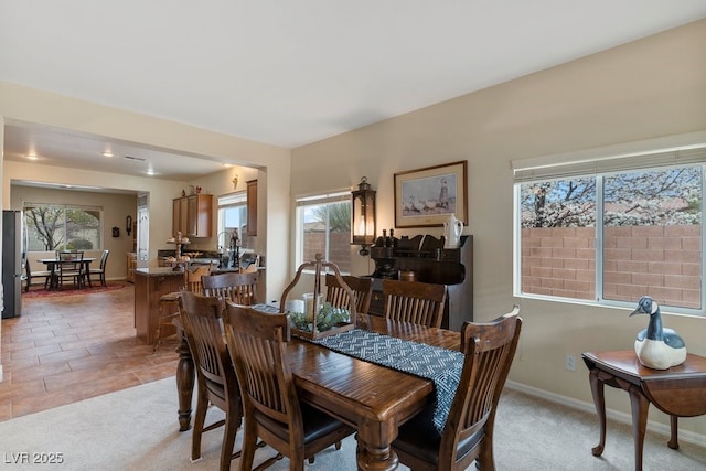 dining area with a wealth of natural light, baseboards, and light carpet