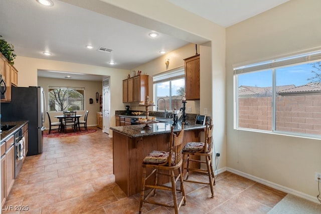 kitchen featuring dark stone countertops, brown cabinetry, baseboards, visible vents, and a sink