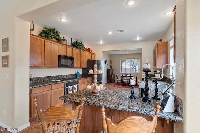 kitchen featuring visible vents, brown cabinets, black appliances, a peninsula, and a breakfast bar area