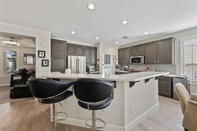 kitchen with washer / dryer, light wood-style flooring, stainless steel appliances, and light countertops