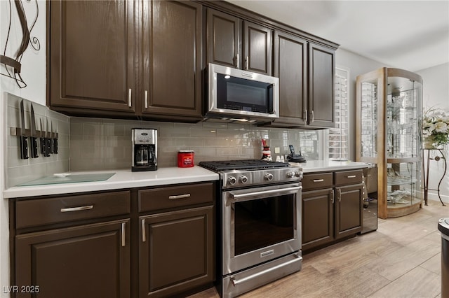 kitchen featuring stainless steel appliances, light countertops, dark brown cabinetry, and tasteful backsplash