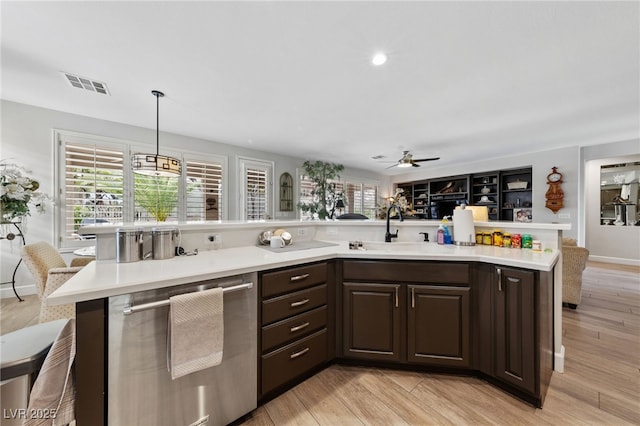 kitchen with light countertops, visible vents, stainless steel dishwasher, dark brown cabinetry, and a sink