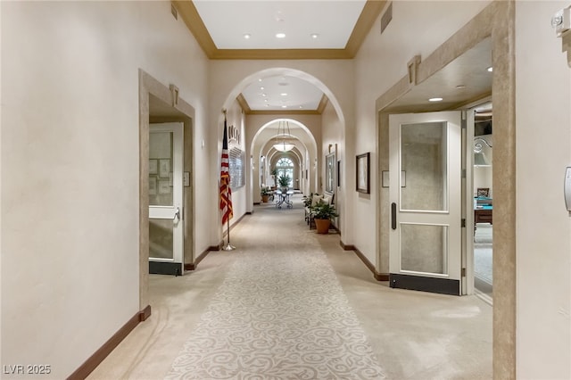 hall featuring light carpet, baseboards, arched walkways, and ornamental molding