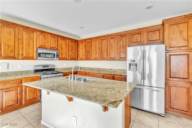 kitchen with light stone counters, light tile patterned floors, appliances with stainless steel finishes, brown cabinetry, and a sink