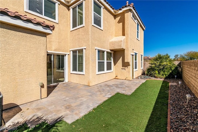 rear view of house with a tile roof, a fenced backyard, a patio, and stucco siding