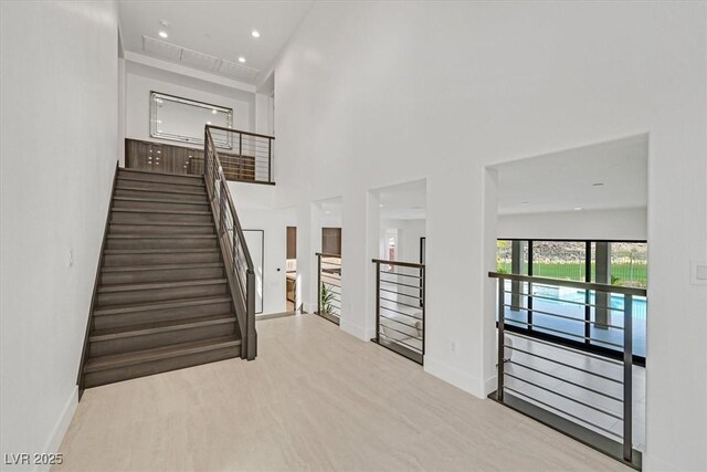 stairway with a high ceiling, baseboards, wood finished floors, and recessed lighting