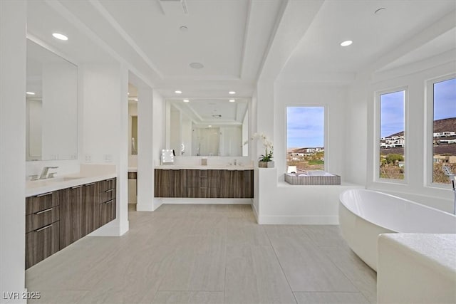 full bathroom featuring a sink, a freestanding tub, baseboards, and two vanities