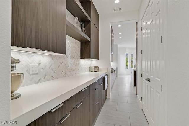 kitchen with visible vents, decorative backsplash, modern cabinets, light countertops, and dark brown cabinets