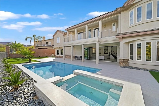 rear view of property featuring a balcony, stone siding, fence, a patio area, and stucco siding