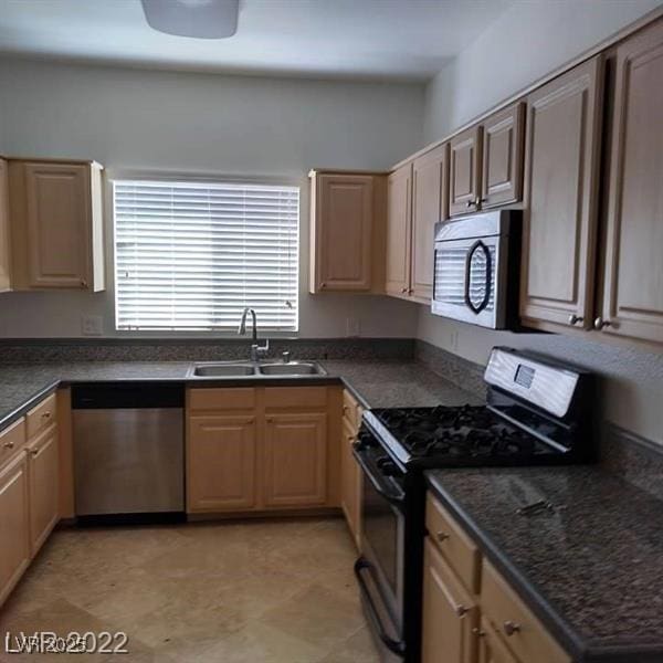 kitchen featuring stainless steel appliances, dark countertops, a sink, and light brown cabinetry