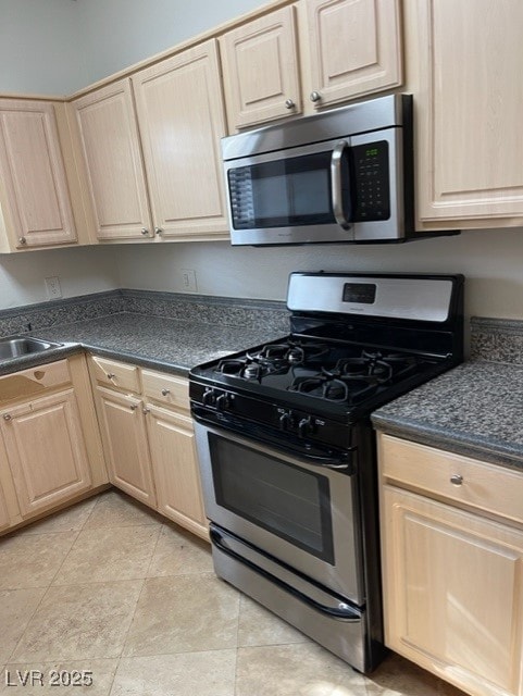 kitchen featuring dark countertops, stainless steel appliances, a sink, and light brown cabinetry