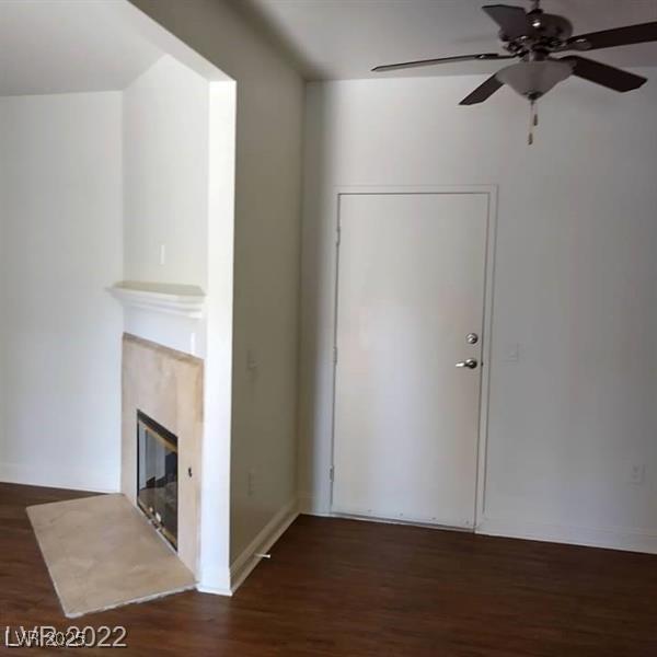 interior space featuring a glass covered fireplace, ceiling fan, baseboards, and wood finished floors