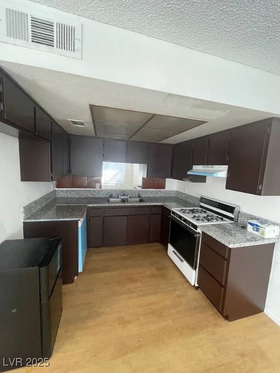 kitchen with visible vents, white gas range, light wood-type flooring, under cabinet range hood, and a sink