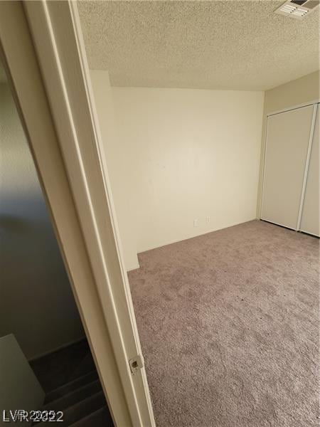 unfurnished bedroom with a textured ceiling, carpet flooring, and visible vents