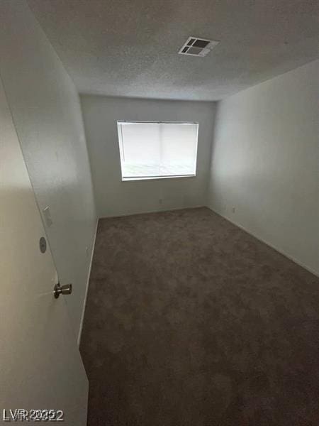 spare room with a textured ceiling, visible vents, and carpet flooring