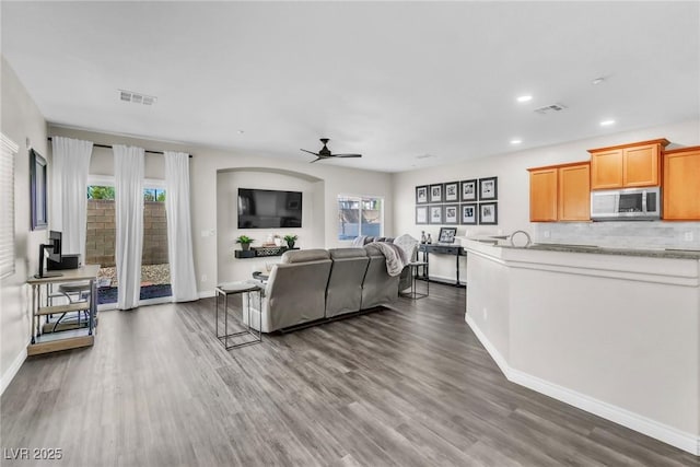 living area featuring a ceiling fan, visible vents, and dark wood finished floors