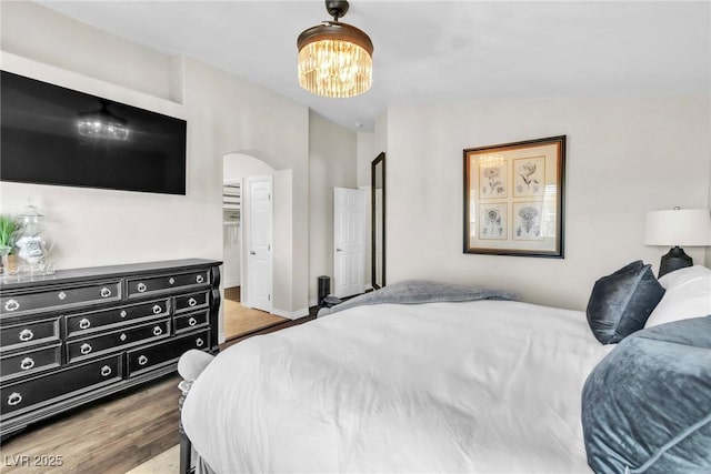 bedroom featuring arched walkways, baseboards, wood finished floors, and an inviting chandelier