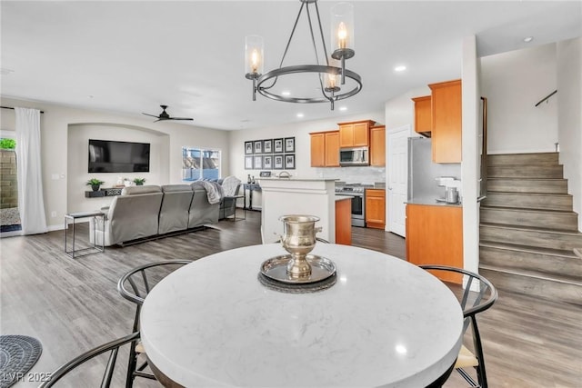 dining space featuring stairs, ceiling fan with notable chandelier, dark wood finished floors, and a healthy amount of sunlight