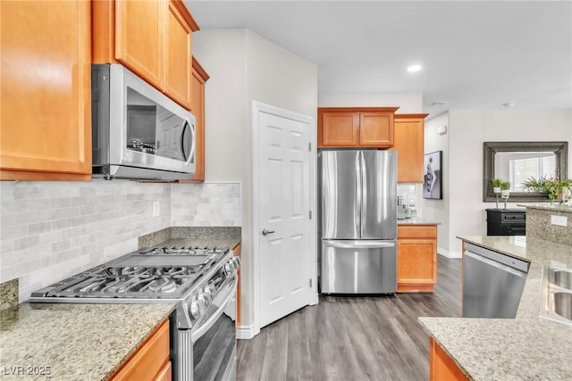 kitchen featuring appliances with stainless steel finishes, tasteful backsplash, light stone counters, and wood finished floors