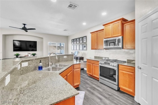 kitchen with visible vents, a sink, stainless steel appliances, light wood-style floors, and backsplash