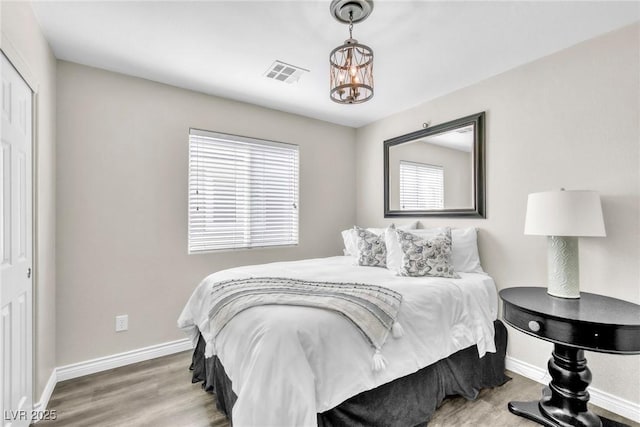 bedroom with an inviting chandelier, visible vents, baseboards, and wood finished floors