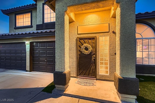 property entrance with stucco siding, driveway, an attached garage, and a tile roof