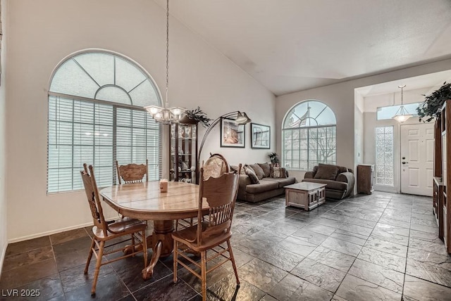 dining room featuring baseboards, high vaulted ceiling, stone tile floors, and a chandelier