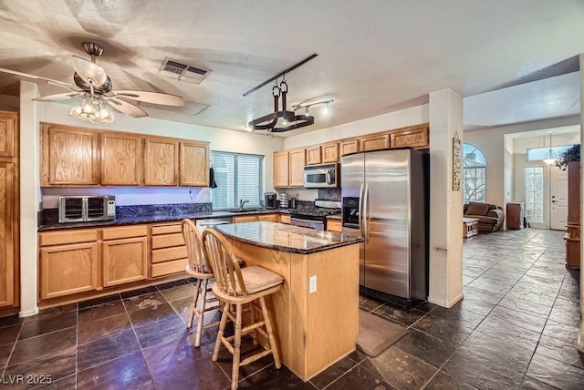 kitchen featuring visible vents, a toaster, appliances with stainless steel finishes, a kitchen bar, and a center island