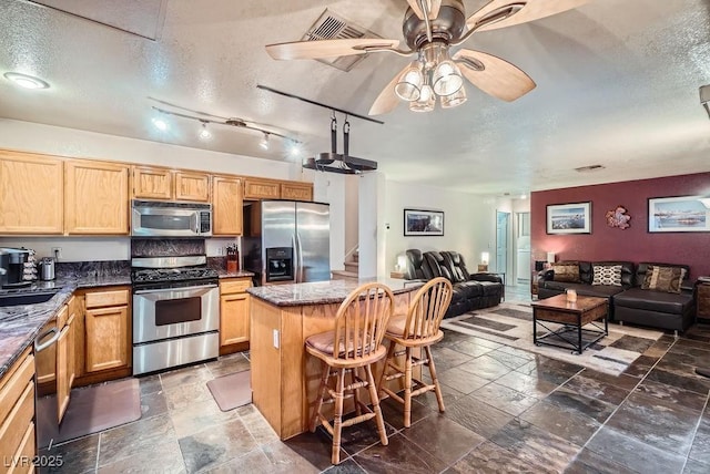 kitchen featuring stone tile floors, appliances with stainless steel finishes, a textured ceiling, open floor plan, and a center island