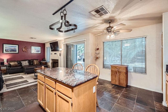 kitchen with visible vents, a center island, ceiling fan, open floor plan, and a fireplace