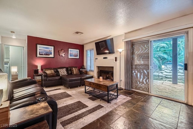 living room with stone tile floors, a fireplace, visible vents, and a textured ceiling