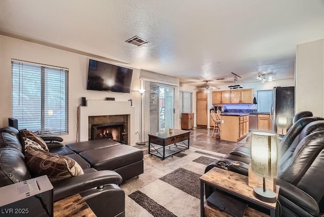 living room featuring a tiled fireplace, visible vents, plenty of natural light, and a textured ceiling