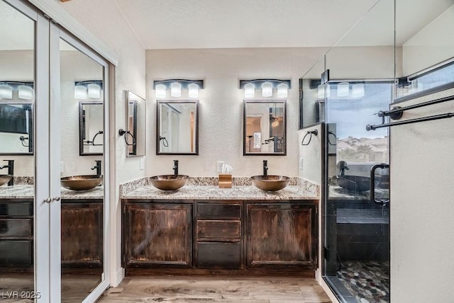 full bath featuring double vanity, wood finished floors, a shower stall, and a sink