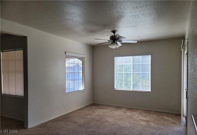 carpeted spare room with a textured ceiling, ceiling fan, baseboards, and a healthy amount of sunlight