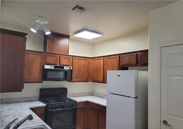 kitchen with visible vents, brown cabinetry, freestanding refrigerator, a sink, and gas stove