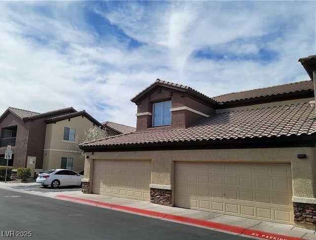 view of front facade featuring a garage, stone siding, a tile roof, and stucco siding