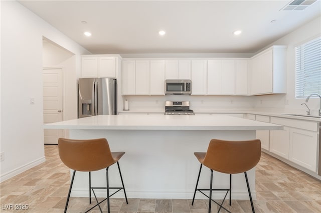 kitchen featuring a breakfast bar area, visible vents, appliances with stainless steel finishes, white cabinetry, and a sink