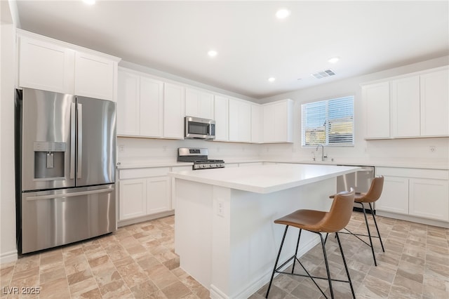 kitchen featuring visible vents, a kitchen breakfast bar, a center island, stainless steel appliances, and white cabinetry