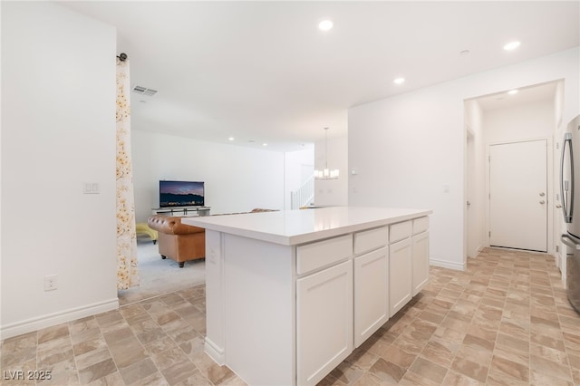 kitchen with light countertops, visible vents, open floor plan, white cabinetry, and a kitchen island