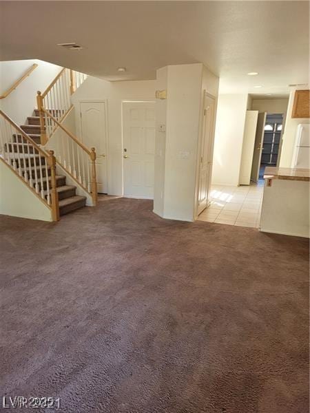 spare room featuring light carpet, stairway, and light tile patterned floors